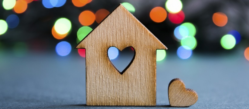 Mini wooden house in front of Christmas lights to represent Austin home sales.