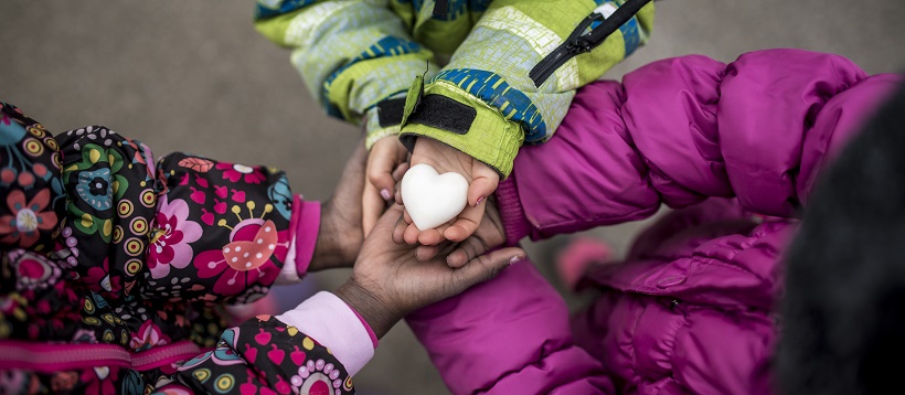 Children wearing coats and holding hands with heart in the middle