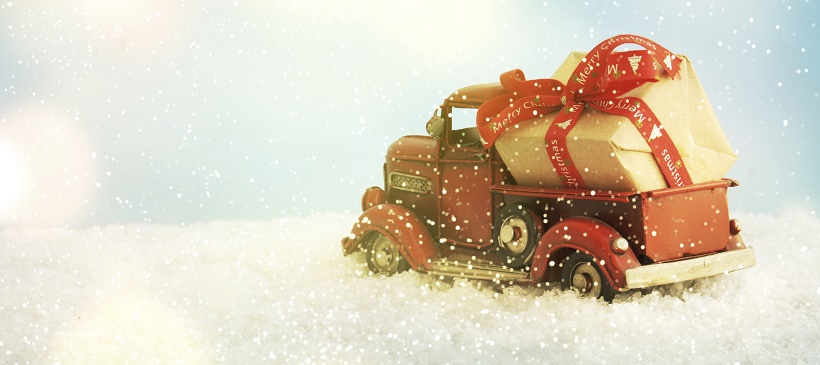 Toy truck carrying Christmas gift through fake snow