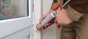 Person caulking window to help with home winterization plan