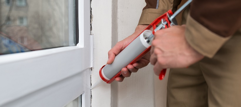 Person caulking window to help with home winterization plan