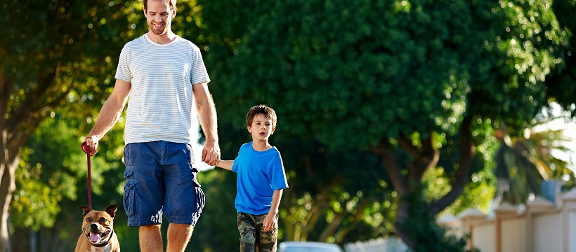 Dad walking with his son and a dog down a suburban street.