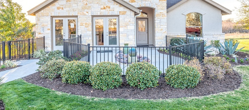 Landscaping and patio encircling the front of a brick exterior new Austin home