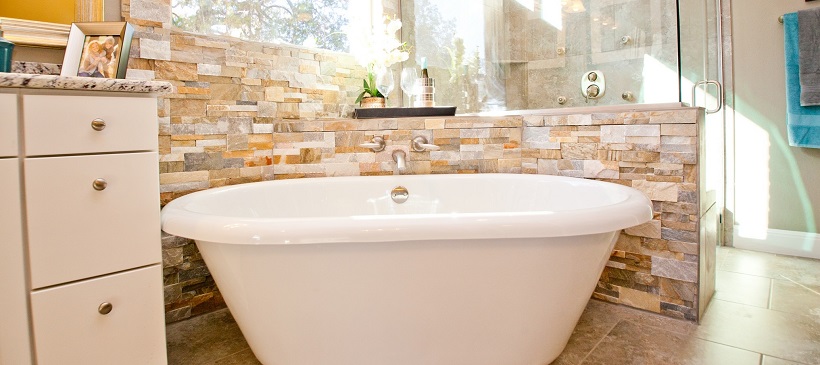 White porcelain tub surrounded by textured stone wall and glass shower in a new Austin home