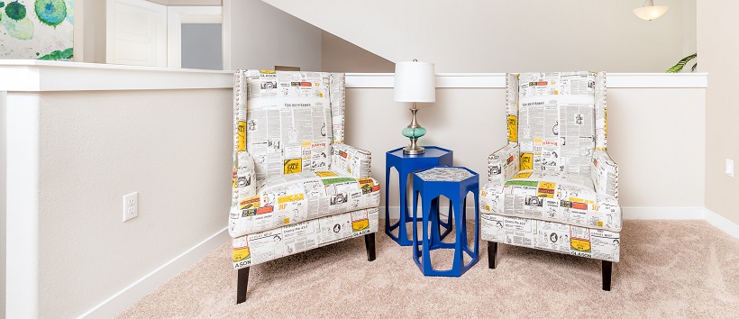 Two bright blue modern end tables between newspaper-patterned armchairs with orange accents. 