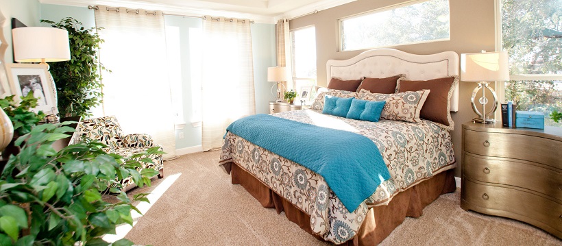 Light streaming in large bedroom with brown and blue bedding on bed.