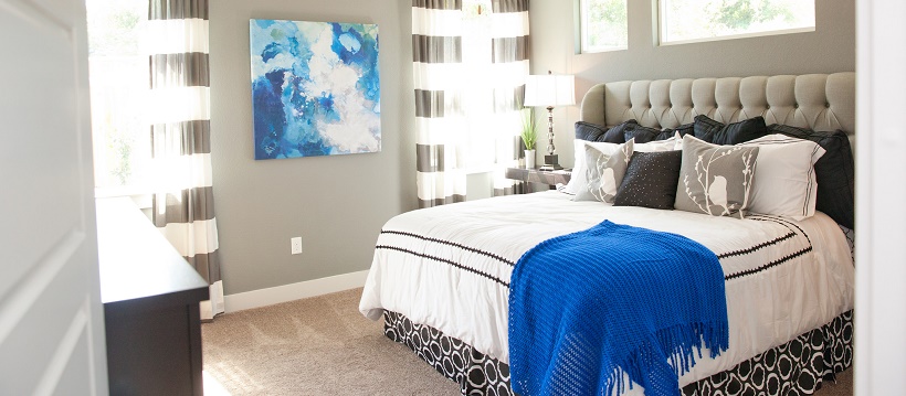 Bedroom with gray walls, a blue and white painting, and a blue throw on a white and black bedspread.