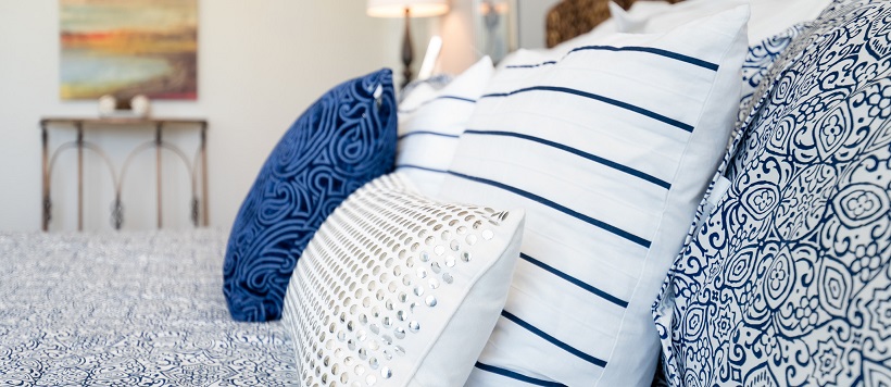 Close up of swirl-patterned blue bedspread with blue and white patterned pillows.