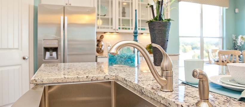 Close up of a stainless steel sink and faucet surrounded by a granite countertop in a blue and white kitchen.