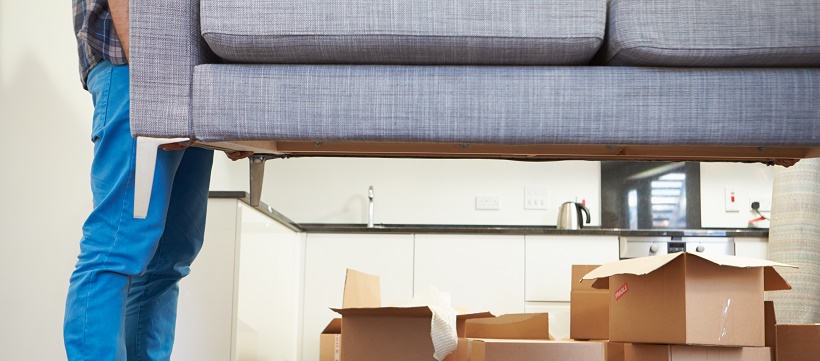 Man lifting couch over cardboard packing boxes as final part of moving timeline.