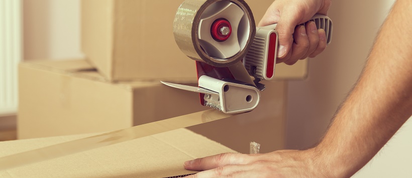 Arm of man holding moving box while taping the ends shut with packing tape.