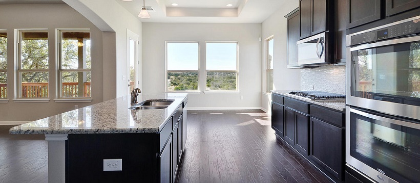 A dark cabinetry kitchen with granite and stainless steel appliances all opening up to a Hill Country view.