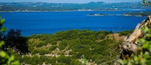 View of bright blue water at Lake Travis surrounded by vibrant green Hill Country.