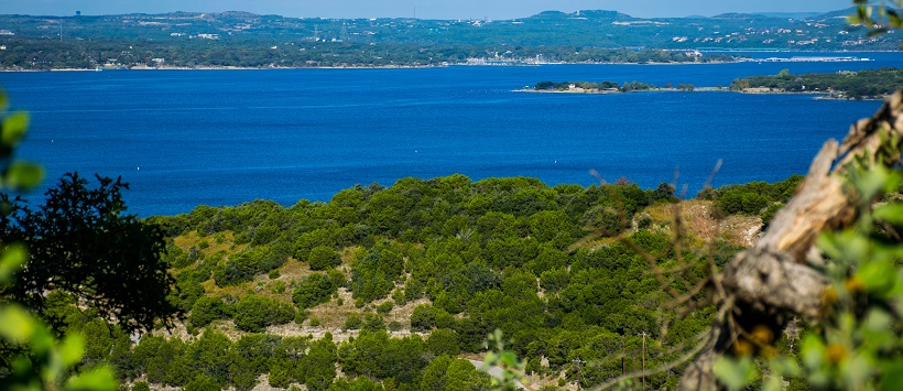 View of bright blue water at Lake Travis surrounded by vibrant green Hill Country.