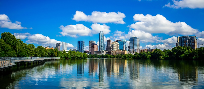 Vibrant blue sky filled and white clouds over an Austin skyline reflected in Lady Bird Lake.