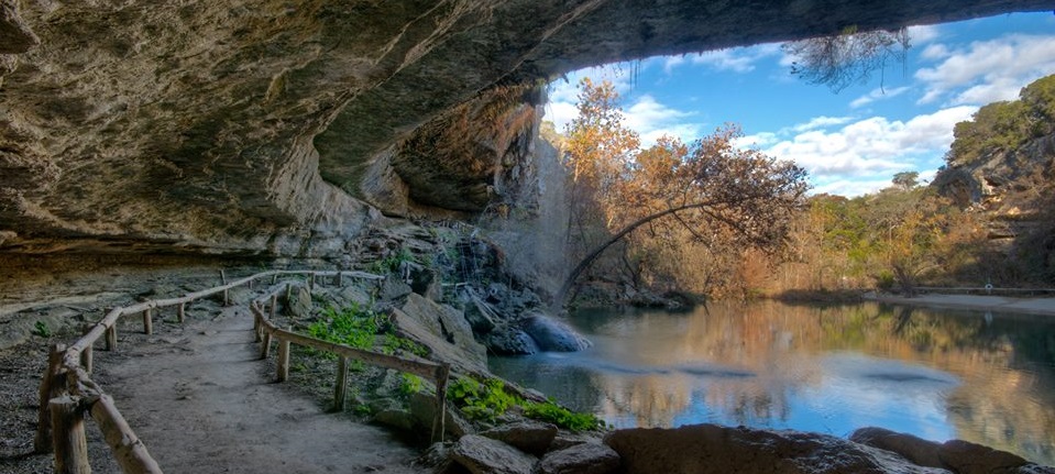 Rock formations create a roof over a walkway that circles around the water at Hamilton Pool.