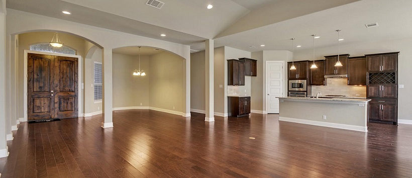 Open floor plan design of entry, dining room, and kitchen with hardwood floors and brown cabinetry throughout.