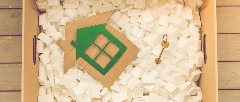 Cardboard box filled with packing material and cutout of green house and key on top of material.