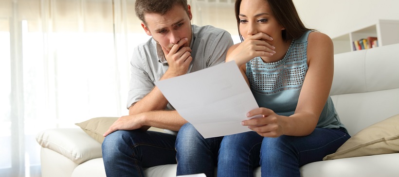 Man and woman looking over a piece of paper with hands over mouths.