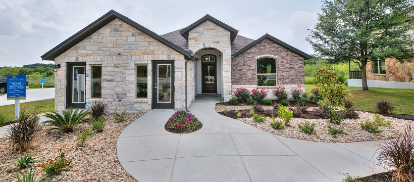 Landscaped yard and sidewalk lead up to a stone and brick front exterior of a one-story home.