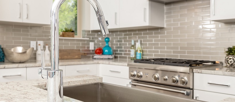 Close up of silver faucet over deep sink with stainless steel oven in the background of kitchen.