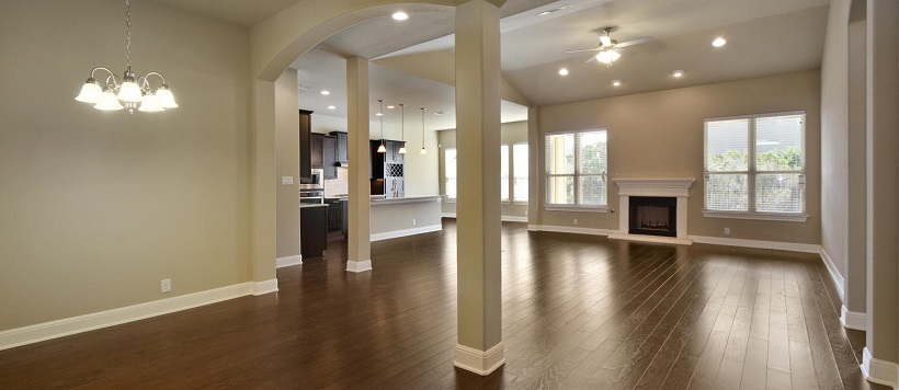 Hardwood floors of a blank open-concept home lead into the kitchen.