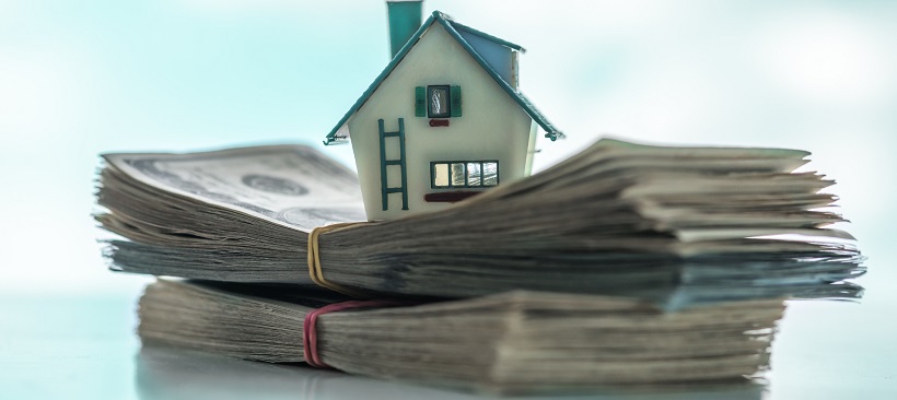 Miniature home sitting on two stacks of dollar bills.