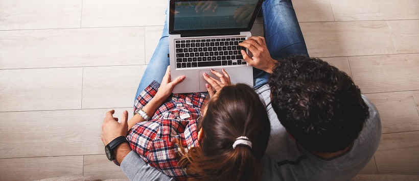 Young couple sitting on the floor and looking at laptop to answer the question, should I rent or buy