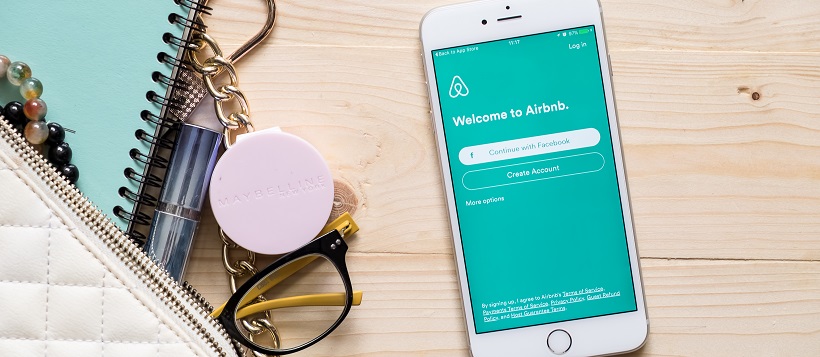 Purse with contents spilled out next to smartphone showing Airbnb screen.