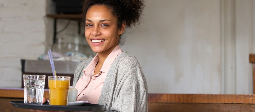 Smiling waitress holding a try with water and a smoothie.