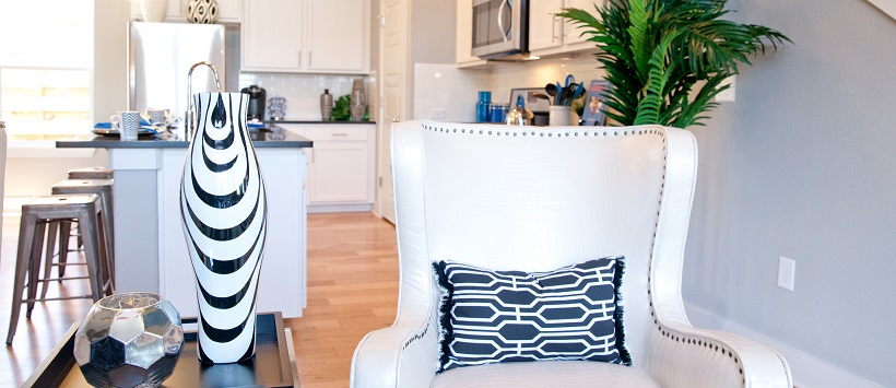 White armchair white black and white pillow and a white kitchen in the background.