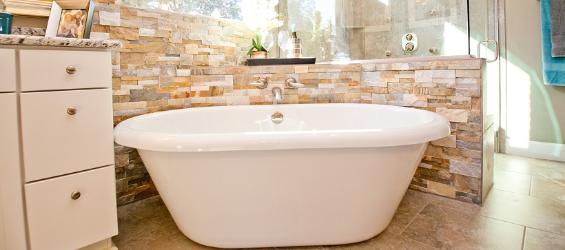 Luxurious bathroom with white porcelain tub surrounded by a stone tiled backsplash.