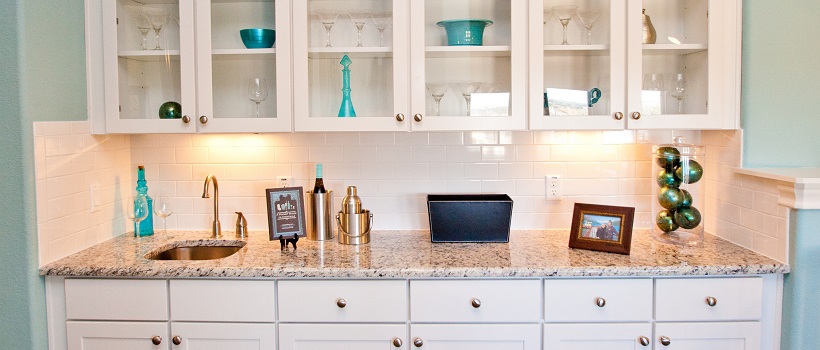 Bar area with white cabinets, granite, and blue home decor pieces inside the cabinetry.