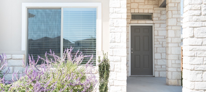 Front home exterior with a window surrounded by white stone leading to the front door.