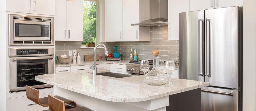 White modern kitchen with stainless steel appliances and white granite on center island.