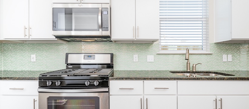 Kitchen with white contemporary cabinetry, stainless steel appliances, and a green backsplash.