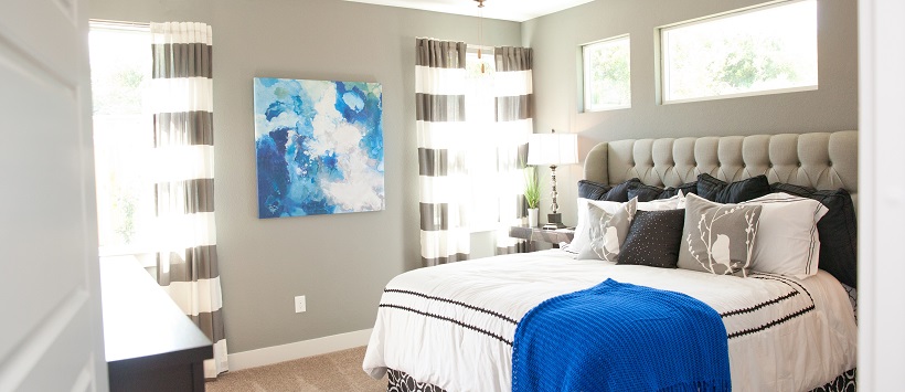 Gray walls surround a large bed with a white bedspread with black accents.