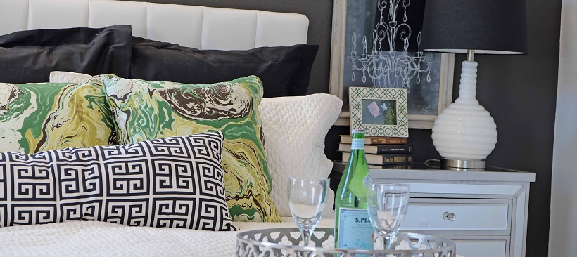 Close up of bed with white bedspread and headboard with black and green pillows between.