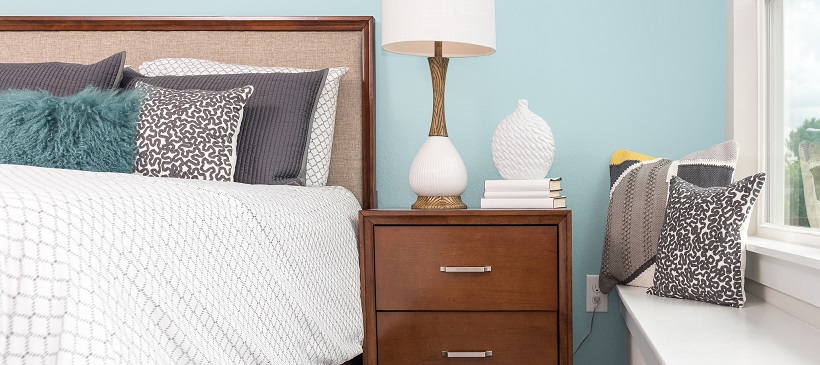 Bedroom with blue walls and a bed with a white bedspread next to a wooden side table with white home decor ideas on top.