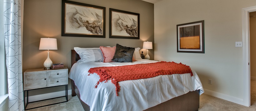 Bed with white bedspread and orange throw in front of tan accent wall.