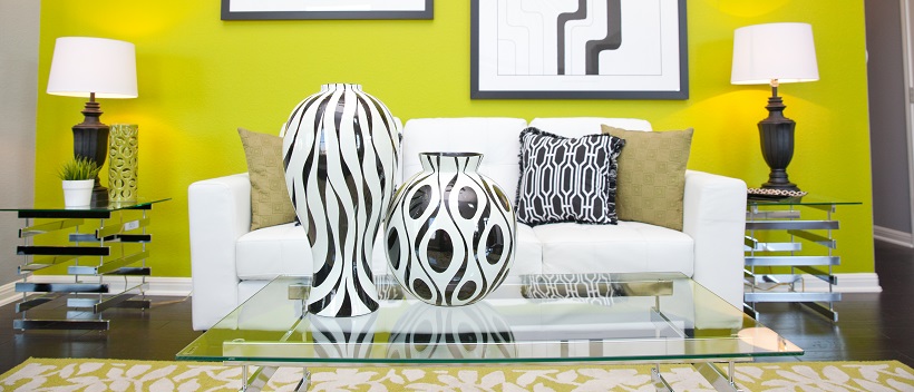 Black and white home decor ideas placed on glass table in front of white couch with vibrant yellow accent wall in the background.