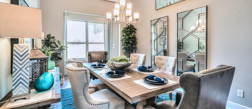 Dining room with luxurious chairs surrounding a wooden table, with a chandelier above, and mirror decor on the walls.