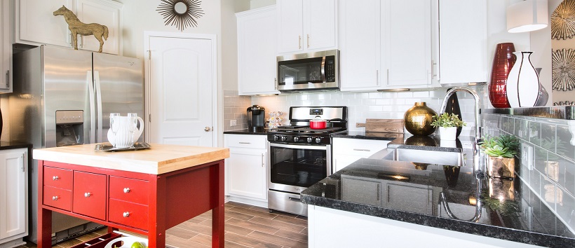 A contemporary white kitchen with black granite and a red island.