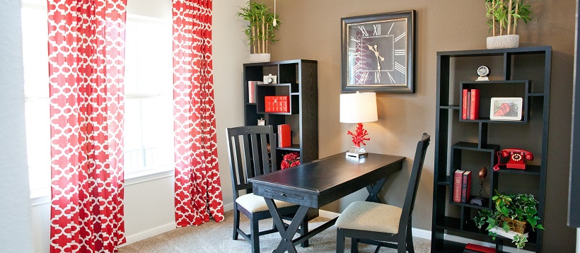 Study with red and white drapes next to a brown accent wall behind bookshelves and a desk.