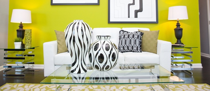 Behind white and black vases sits a white couch in front of a vibrant yellow wall.