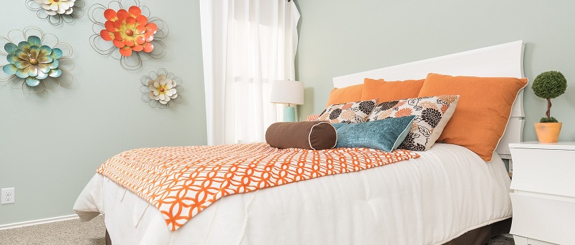 A gray-blue painted bedroom with a bed topped by orange blankets and pillows.