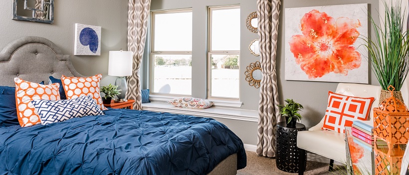 Bed topped by a blue bedspread and white and orange pillows, surrounded by orange and white decor.