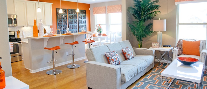 Gray and orange living room in front of a white and orange kitchen.