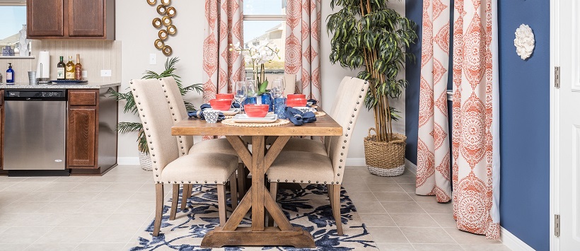 Dining room with a wooden table topped by red and blue china, next to a blue accent wall with red and white drapes.