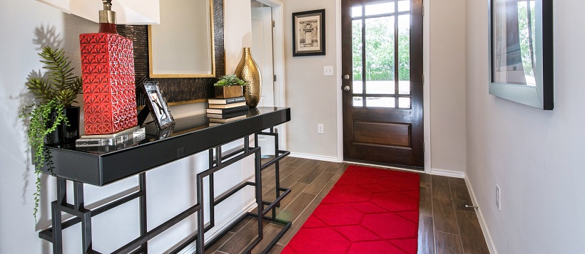 Entryway with thin red rug near a side table with a red lamp. 